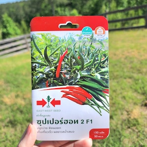 May include: A red and white seed packet with a picture of red and green chili peppers. The packet is labeled "Super Hot 2 F1" and says "Easy to grow, high yield, fast harvest".