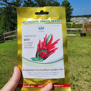 May include: A gold packet of F1 Hybrid Cluster Hot Chilli seeds. The packet features a red and green chili pepper illustration and the text "Golden Hot" in English and Thai.