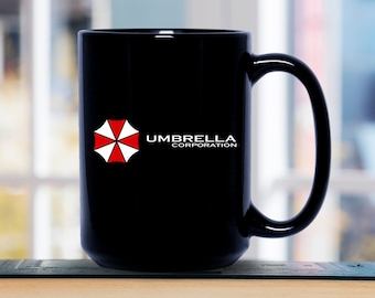 Peut inclure: Une tasse en céramique noire avec un logo blanc d'Umbrella Corporation, comportant un symbole de parapluie rouge et blanc. La tasse est posée sur une pile de livres.