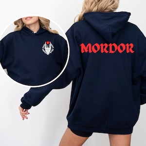 Könnte beinhalten: Ein marineblauer Kapuzenpullover mit einer weißen Grafik auf der Vorderseite und dem Wort "MORDOR" in Rot auf der Rückseite.
