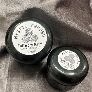 May include: Two black jars of Mystic Ground TattWorx Balm, one labeled 4 oz (113ml) and the other 2 oz. The labels are white with the brand name and a triple spiral design.