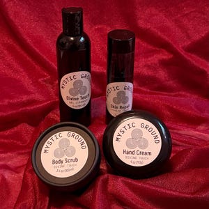 May include: Four black cosmetic containers with white labels. Products include gel cleanser, skin repair, body scrub (100ml), and hand cream (113g). Labels read "Mystic Ground" and "Divine Touch". Set against a red background.