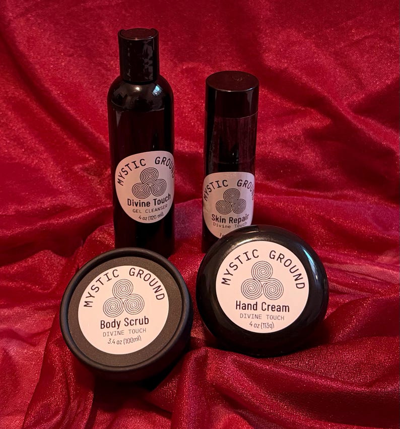 May include: Four black cosmetic containers with white labels. Products include gel cleanser, skin repair, body scrub (100ml), and hand cream (113g). Labels read "Mystic Ground" and "Divine Touch". Set against a red background.