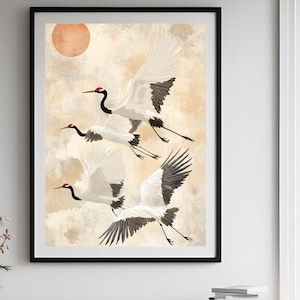 Puede incluir: Una impresión enmarcada de una pintura minimalista de acuarela con tres grullas blancas en vuelo sobre un fondo beige con un suave sol naranja.