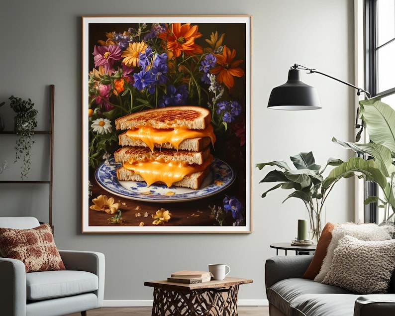 K&ouml;nnte beinhalten: Gerahmter Kunstdruck mit einem Stapel von drei gegrillten K&auml;sesandwiches auf einem blau-wei&szlig;en Teller. Die Sandwiches haben geschmolzenen K&auml;se und sind vor einem Hintergrund aus bunten Blumen platziert.