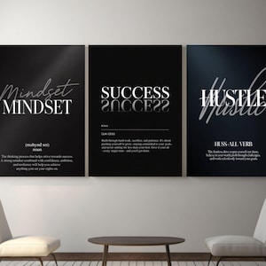 Op de afbeelding: Drie ingelijste, motiverende kunstprints met zwarte achtergronden en witte tekst. De prints tonen de woorden "Mindset", "Success" en "Hustle" in stijlvolle lettertypen. De prints worden weergegeven boven een kleine tafel en twee witte stoelen.