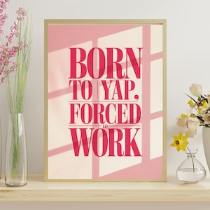 Può includere: Una stampa incorniciata con la scritta "BORN TO YAP, FORCED TO WORK" in un carattere rosa intenso. La stampa è ambientata su uno sfondo rosa con ombre di finestre. La cornice è dorata. La stampa è su una mensola di legno con vasi di fiori.
