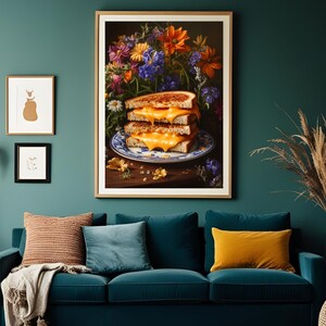 K&ouml;nnte beinhalten: Ein gerahmter Kunstdruck zeigt einen Stapel von drei gegrillten K&auml;sesandwiches auf einem blau-wei&szlig;en Teller, vor einem Hintergrund aus bunten Blumen. Das Kunstwerk h&auml;ngt &uuml;ber einem teal-farbenen Sofa mit Kissen und schafft eine gem&uuml;tliche Wohnzimmerszene.
