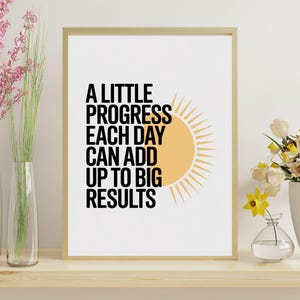 May include: A framed print with the text "A Little Progress Each Day Can Add Up To Big Results" in black, with a yellow sun graphic. The print is displayed on a wooden shelf with vases of pink and yellow flowers.
