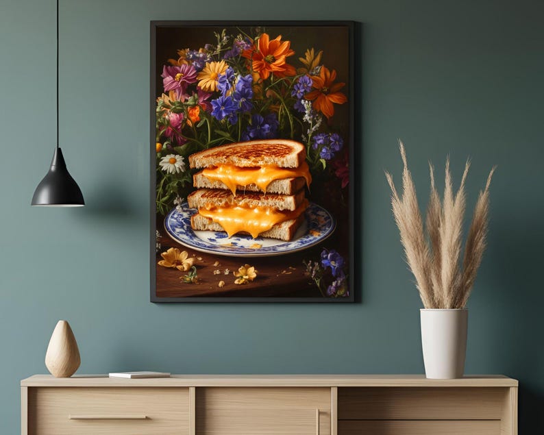 K&ouml;nnte beinhalten: Gerahmter Kunstdruck mit einem Stapel von drei gegrillten K&auml;sesandwiches mit geschmolzenem K&auml;se auf einem blau-wei&szlig;en Teller. Ein lebendiger Blumenstrau&szlig; im Hintergrund.