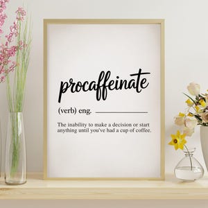 May include: A framed print with the word "procaffeinate" in black script. The definition below reads: "The inability to make a decision or start anything until you've had a cup of coffee." The frame is gold.