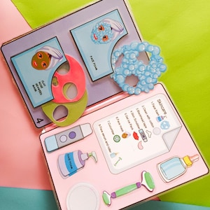 Könnte beinhalten: Ein Set zum Thema Hautpflege mit illustrierten Karten und Zubehör. Enthält Gesichtsmasken, Gesichtsschaum, eine Jaderolle und eine Gurkengrafik. Das Set befindet sich auf einem rosa-grünen Hintergrund.