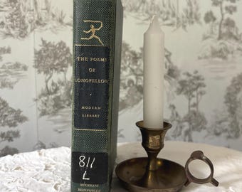 May include: A vintage book titled "The Poems of Longfellow" with a green cover and gold lettering, next to a brass candlestick holding a white candle. The background features a patterned wallpaper.