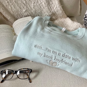 Peut inclure: Sweat-shirt bleu clair avec le texte "shhh... i'm on a date with my book boyfriend" brod&eacute; sur le devant. Le sweat-shirt pr&eacute;sente une petite image brod&eacute;e d'un livre.