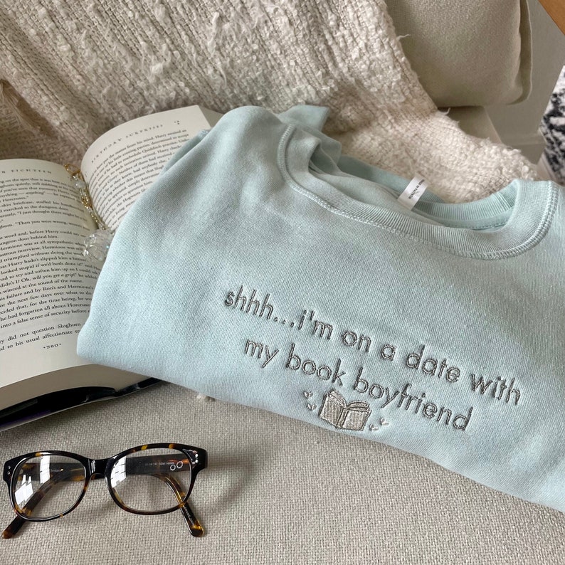Peut inclure: Sweat-shirt bleu clair avec le texte "shhh... i'm on a date with my book boyfriend" brod&eacute; sur le devant. Le sweat-shirt pr&eacute;sente une petite image brod&eacute;e d'un livre.