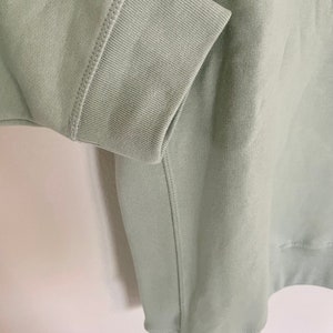 Peut inclure: Un sweat-shirt vert sauge avec un poignet c&ocirc;tel&eacute; et une couture sur le c&ocirc;t&eacute;.