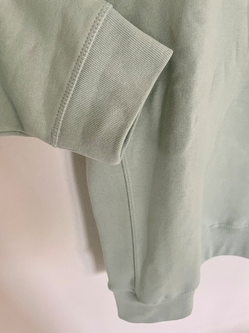 Peut inclure: Un sweat-shirt vert sauge avec un poignet c&ocirc;tel&eacute; et une couture sur le c&ocirc;t&eacute;.