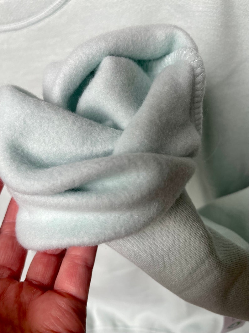 Peut inclure: Gros plan sur un sweat-shirt bleu clair avec un int&eacute;rieur doux et duveteux. Le tissu est pli&eacute; pour montrer l'int&eacute;rieur du v&ecirc;tement.