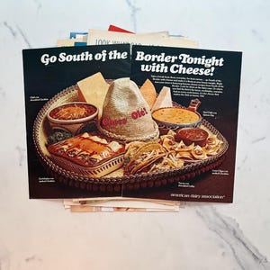 K&ouml;nnte beinhalten: Zwei Vintage-Magazinseiten mit den Schlagzeilen "Go South of the Border Tonight with Cheese!" und "Chees Ol&eacute;!". Die Seiten zeigen ein Tablett mit mexikanischem Essen, darunter Enchiladas, Tacos und K&auml;sedips.