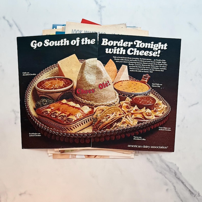 K&ouml;nnte beinhalten: Zwei Vintage-Magazinseiten mit den Schlagzeilen "Go South of the Border Tonight with Cheese!" und "Chees Ol&eacute;!". Die Seiten zeigen ein Tablett mit mexikanischem Essen, darunter Enchiladas, Tacos und K&auml;sedips.
