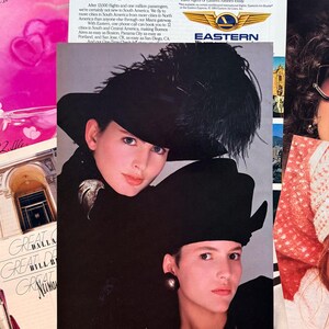 K&ouml;nnte beinhalten: Zwei Frauen in schwarzen H&uuml;ten mit Federakzenten und dunkler Kleidung. Eine Frau tr&auml;gt eine silberne Brosche. Das Bild stammt aus einer alten Zeitschrift mit Text von Eastern Airlines und Neiman Marcus.