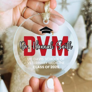 May include: A clear glass ornament with a red "DVM" and the text "Dr. Hannah Smith" in black. Below the text is "UC Davis School of Veterinary Medicine Class of 2025".