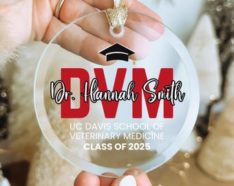 May include: A clear glass ornament with a red "DVM" and the text "Dr. Hannah Smith" in black. Below the text is "UC Davis School of Veterinary Medicine Class of 2025".