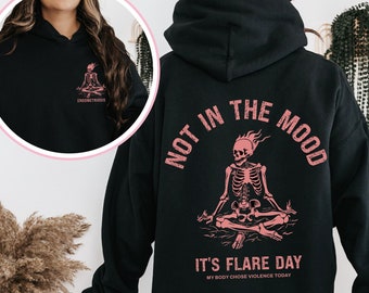 May include: Black hooded sweatshirt with a pink skeleton graphic and the text "Not in the mood, it's flare day, my body chose violence today".