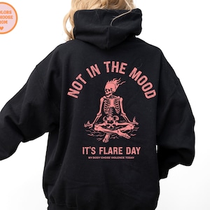unisex chronic illness hoodie in color black. Graphic of a pink skeleton in flames with a phrase not in the mood its flare day in grunge font in pink.