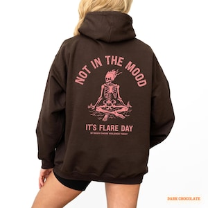 unisex chronic illness hoodie in color dark chocolate. Graphic of a pink skeleton in flames with a phrase not in the mood its flare day in grunge font in pink.