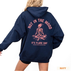 unisex chronic illness hoodie in color navy. Graphic of a pink skeleton in flames with a phrase not in the mood its flare day in grunge font in pink.