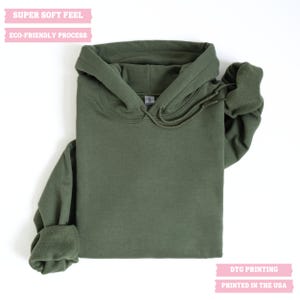 Pu&ograve; includere: Una felpa con cappuccio verde con coulisse. Il testo "SUPER SOFT FEEL" e "ECO-FRIENDLY PROCESS" &egrave; stampato sulla parte superiore della felpa. Il testo "DTG PRINTING" e "PRINTED IN THE USA" &egrave; stampato sulla parte inferiore della felpa.