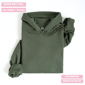 May include: A green hooded sweatshirt with a drawstring. The text "SUPER SOFT FEEL" and "ECO-FRIENDLY PROCESS" is printed on the top of the sweatshirt. The text "DTG PRINTING" and "PRINTED IN THE USA" is printed on the bottom of the sweatshirt.