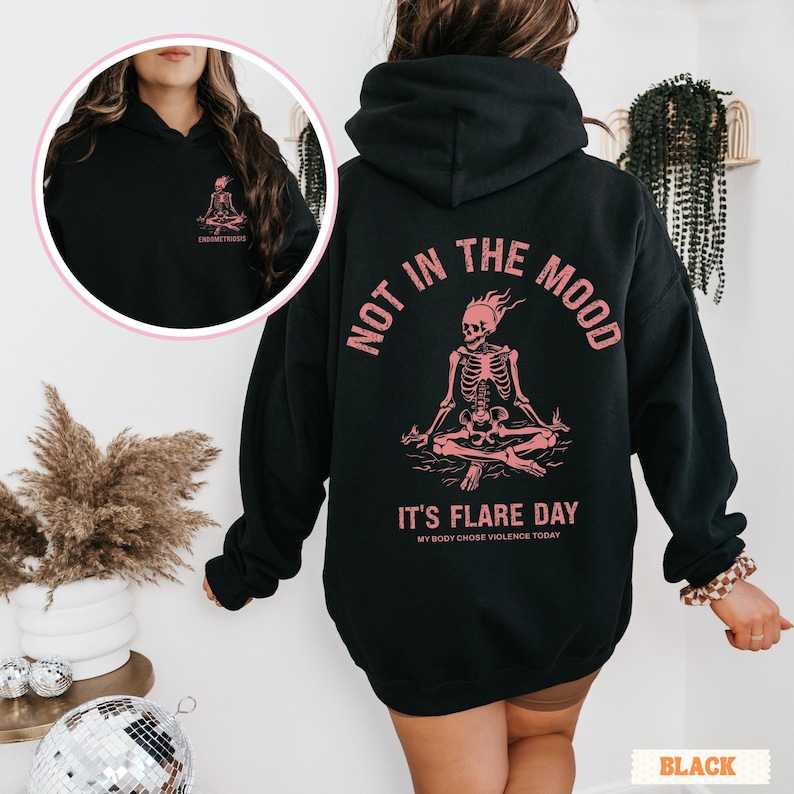 unisex chronic illness hoodie in color black. Back design: Graphic of a pink skeleton in flames with a phrase not in the mood its flare day in grunge font in pink. Pocket design: the same skeleton with the text Endometriosis