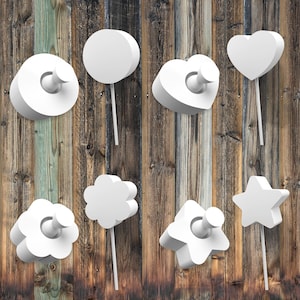 May include: White wooden shapes in the form of a circle, heart, star, and flower, each with a push pin in the center, mounted on a wooden wall.