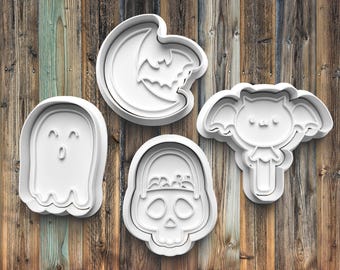 May include: Set of four white plastic Halloween cookie cutters. The cutters are shaped like a ghost, a skull, a bat, and a crescent moon with a bat inside.
