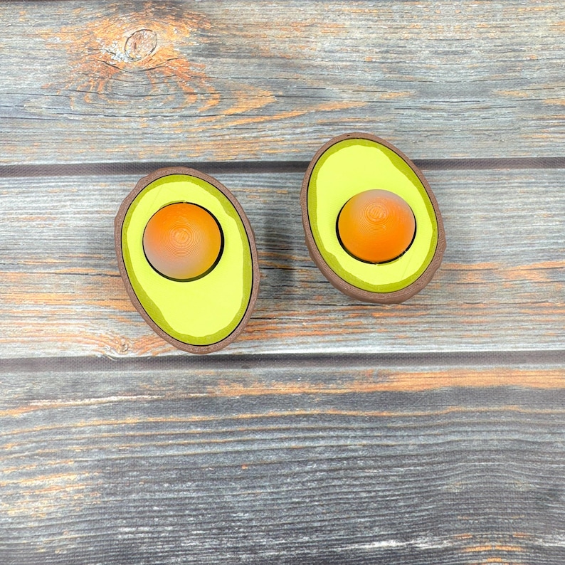 May include: Two wooden avocado halves with yellow interiors and orange pit centers. The avocado halves are on a wood background.