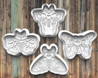 May include: Four white butterfly-shaped cookie cutters with intricate wing and body details are arranged on a wooden surface. The cutters vary in design, showcasing different butterfly species. The background is a rustic wooden plank.