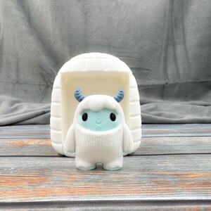 May include: A white 3D printed figurine of a yeti standing in front of a white 3D printed igloo.