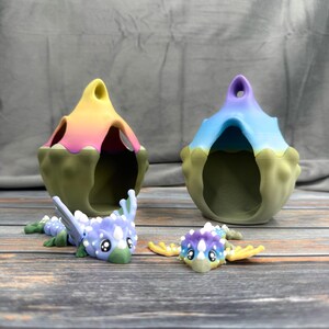 May include: Two colorful, fantasy-themed decorative pieces. Two dragon-like figurines with wings and large eyes are in front of two pod-shaped structures. The structures are in shades of green, yellow, pink, and blue. The figurines are blue, purple, and yellow.