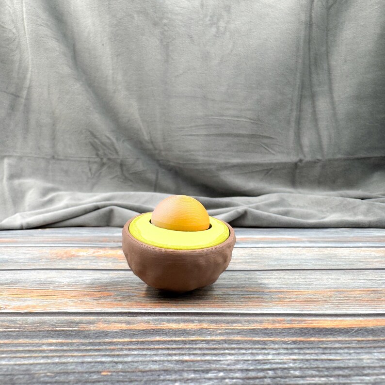 May include: A brown avocado-shaped ceramic egg holder with a yellow avocado pit and a yellow egg inside.