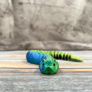 May include: A green and blue segmented toy snake with a detailed head and a textured surface.