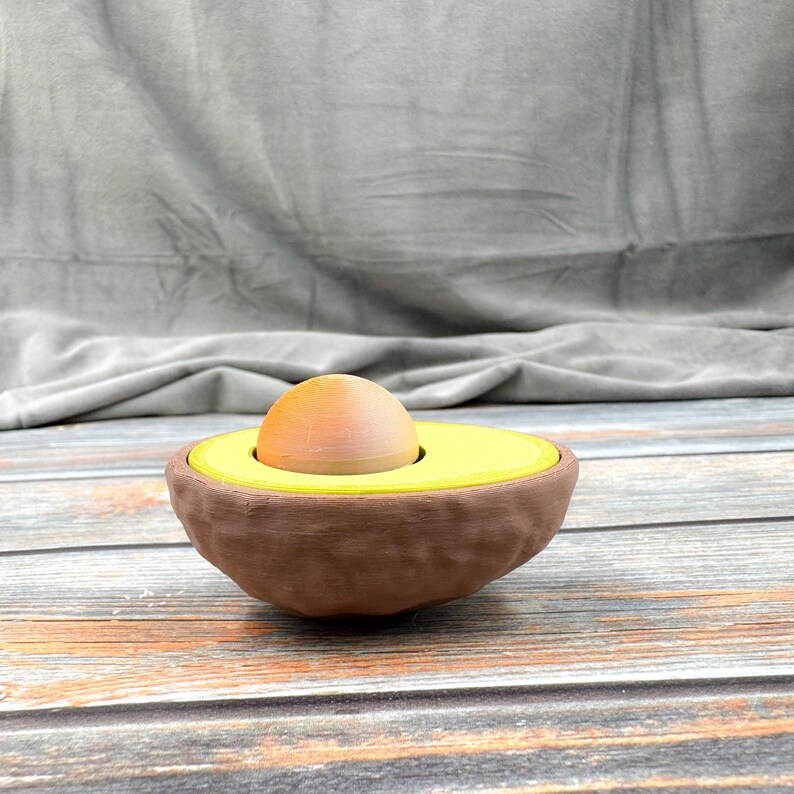 May include: A brown avocado-shaped egg holder with a yellow avocado pit and a brown egg inside.
