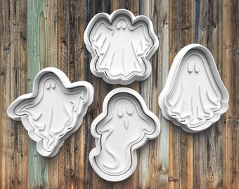 May include: Four white plastic ghost-shaped cookie cutters on a wood background.