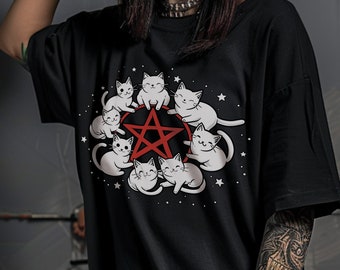 May include: Black t-shirt with a graphic of white cats surrounding a red pentagram. The cats are cartoon-style and have smiling faces.