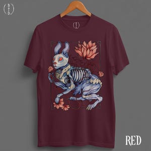 May include: Burgundy t-shirt featuring a detailed illustration of a skeletal rabbit with blue fur and red eyes, surrounded by pink flowers and a lotus. The word "RED" is printed in white on the bottom right.