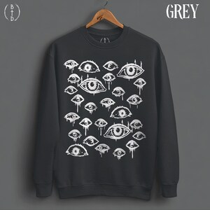 May include: A dark grey crewneck sweatshirt featuring a white graphic print of numerous eyes of varying sizes. Many of the eyes have dripping lines extending downward. The word GREY is printed in the upper right corner, and a logo is in the upper left.