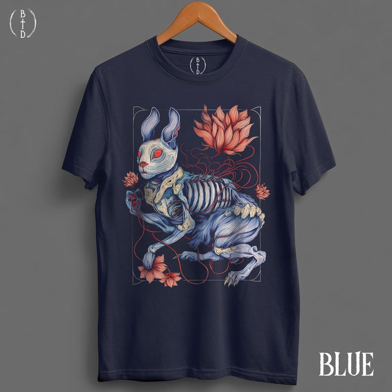 May include: Navy blue t-shirt featuring a detailed illustration of a rabbit skeleton with red eyes, surrounded by flowers and a lotus. The word "BLUE" is printed at the bottom right corner of the shirt.