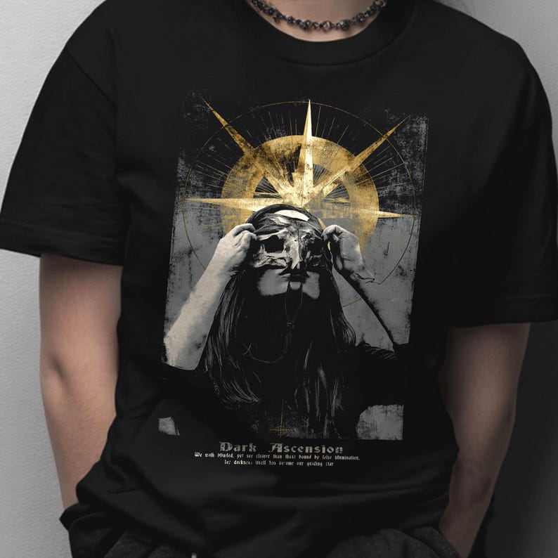 Puede incluir: Camiseta negra con un dise&ntilde;o gr&aacute;fico que presenta a una persona con una m&aacute;scara, con un dise&ntilde;o dorado en forma de br&uacute;jula en el fondo. El texto "Dark Ascension" est&aacute; impreso en la parte inferior.