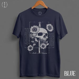 May include: Navy blue t-shirt featuring a detailed skull design pierced by a sword, surrounded by sunflowers. The graphic includes the text "Skulls and Flowers" and is set within a rectangular frame. The word "BLUE" is at the bottom.